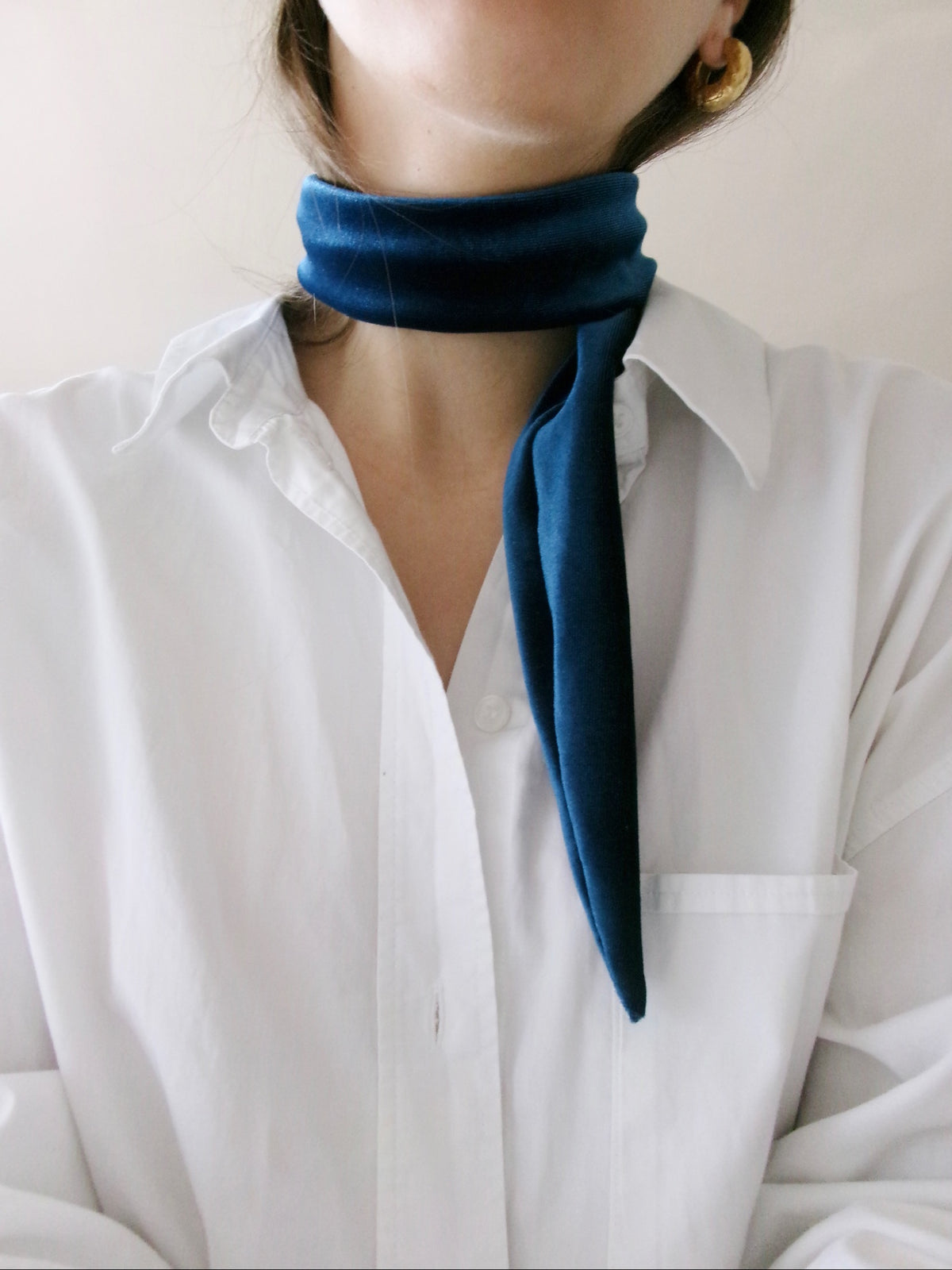 A close-up of a person wearing a dark navy blue velvet neck scarf tied around the collar of a white button-down shirt.
