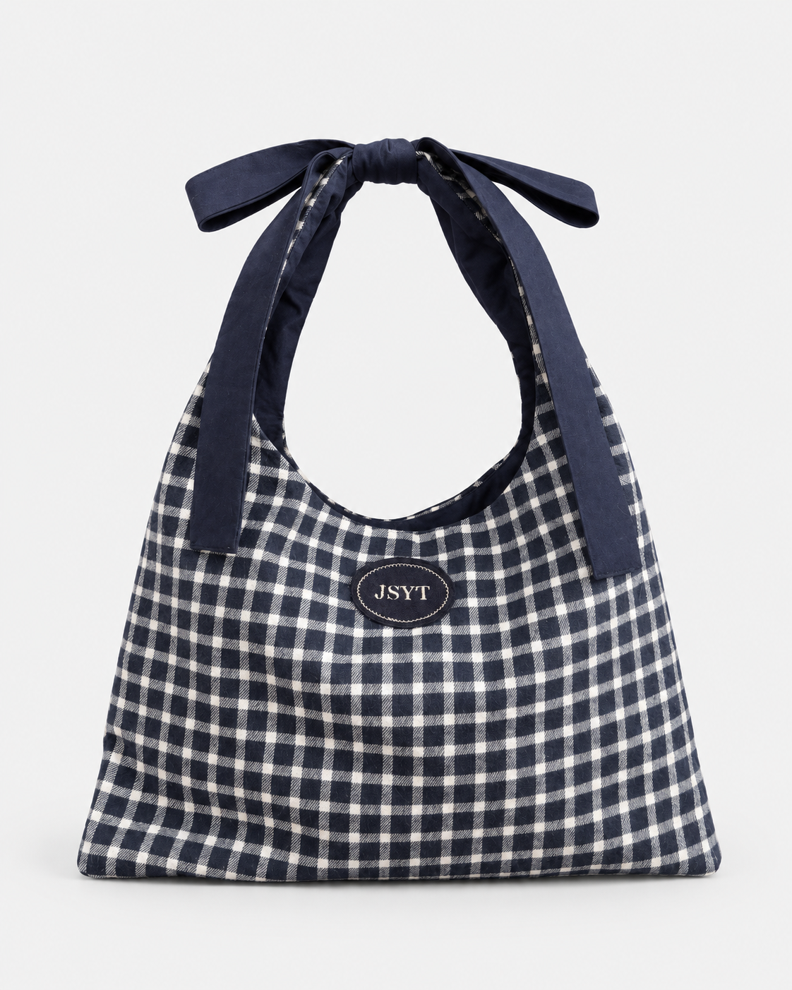 A navy and white gingham tote bag with dark navy fabric shoulder straps tied at the top, featuring a small oval JSYT logo patch on the front, set against a plain light gray background.