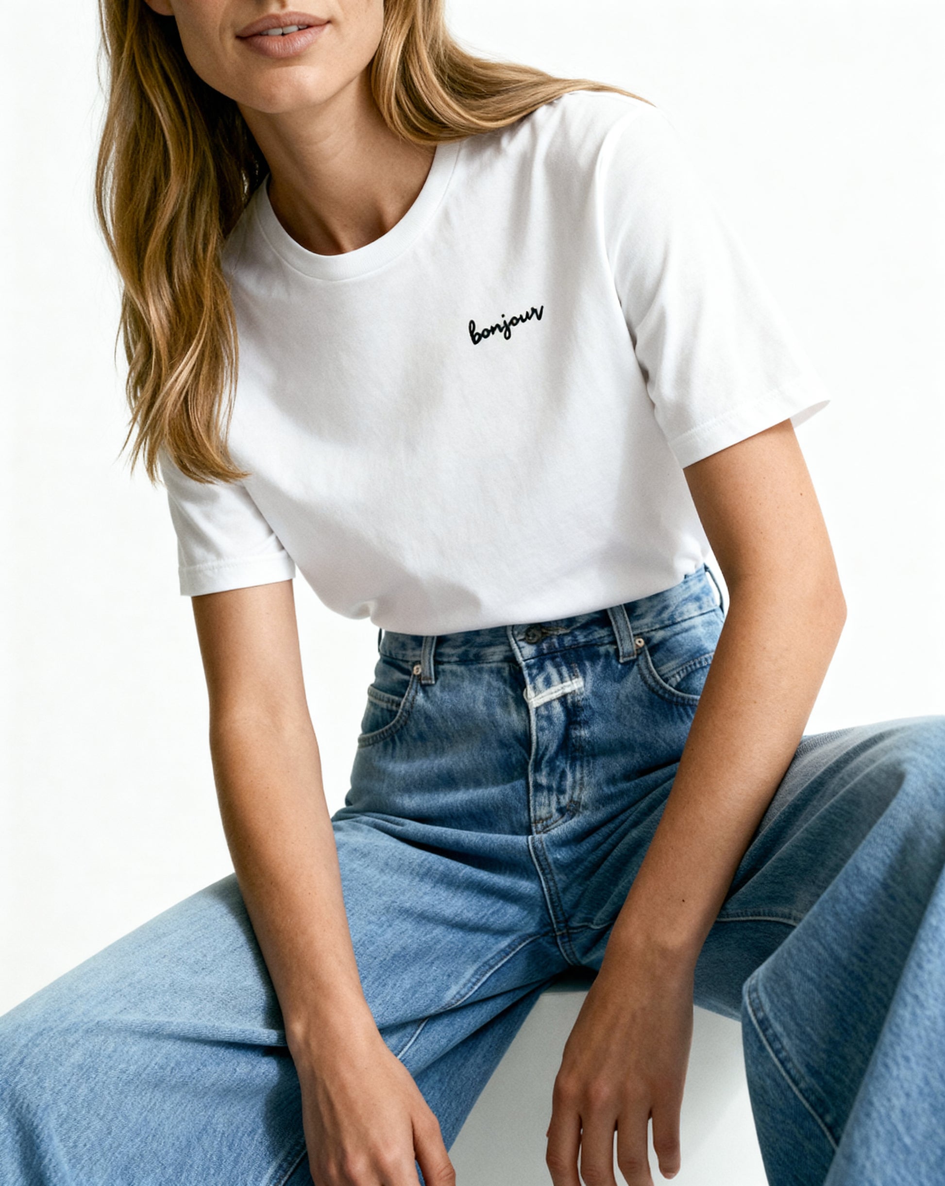 Person wearing a white t-shirt with 'bonjour' text and blue jeans on a white background
