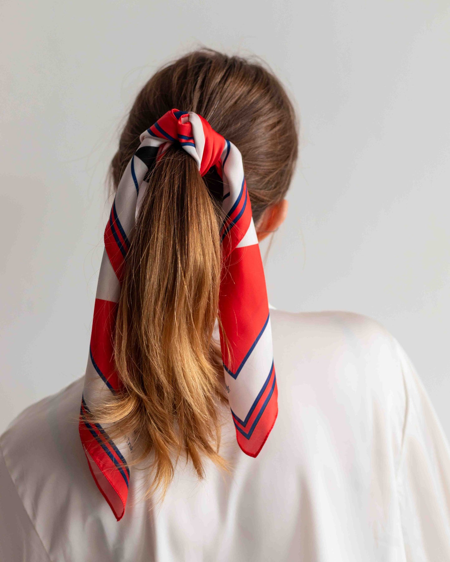Person with a ponytail wearing a red, white, and blue striped hair scarf on a plain background