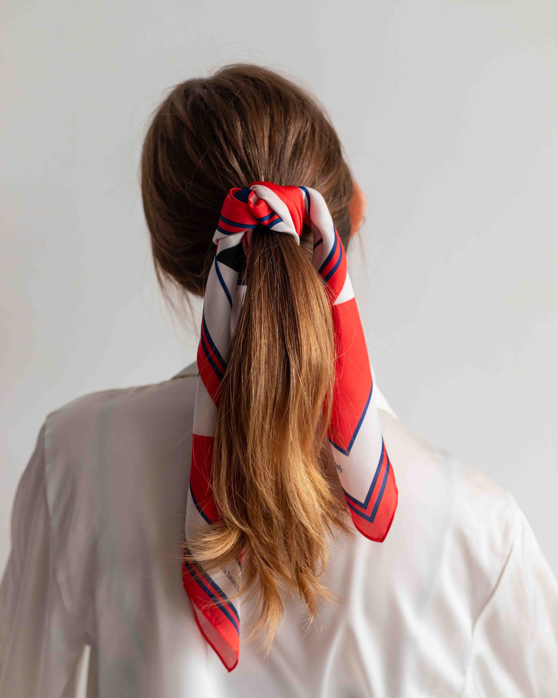 Person with a ponytail wrapped with a red, white, and blue patterned hair tie against a plain background