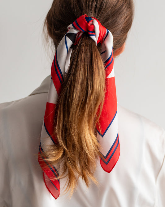 Person with a ponytail wrapped with a red, white, and blue patterned scarf on a plain background