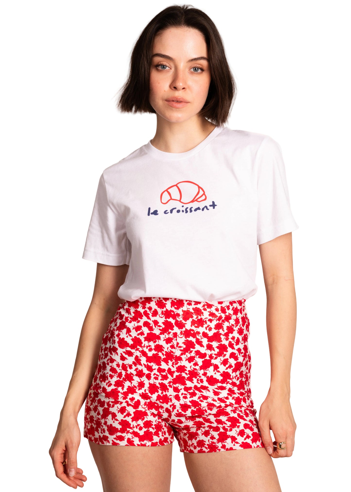 Woman wearing a white t-shirt with a logo and red floral shorts on a light background