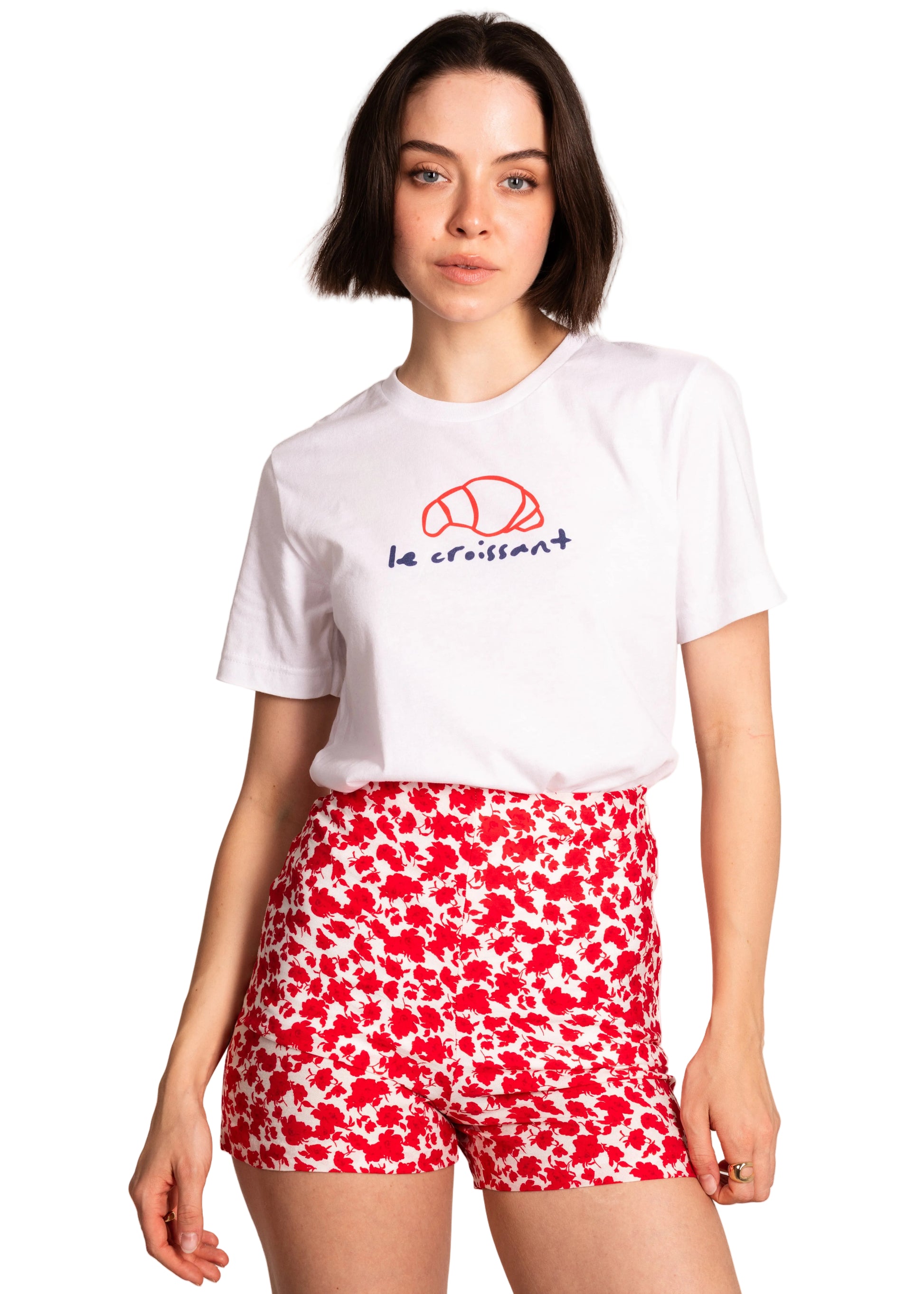 Woman wearing a white t-shirt with a logo and red floral shorts on a light background