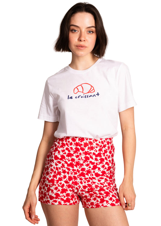 Woman wearing a white t-shirt with a logo and red floral shorts on a light background