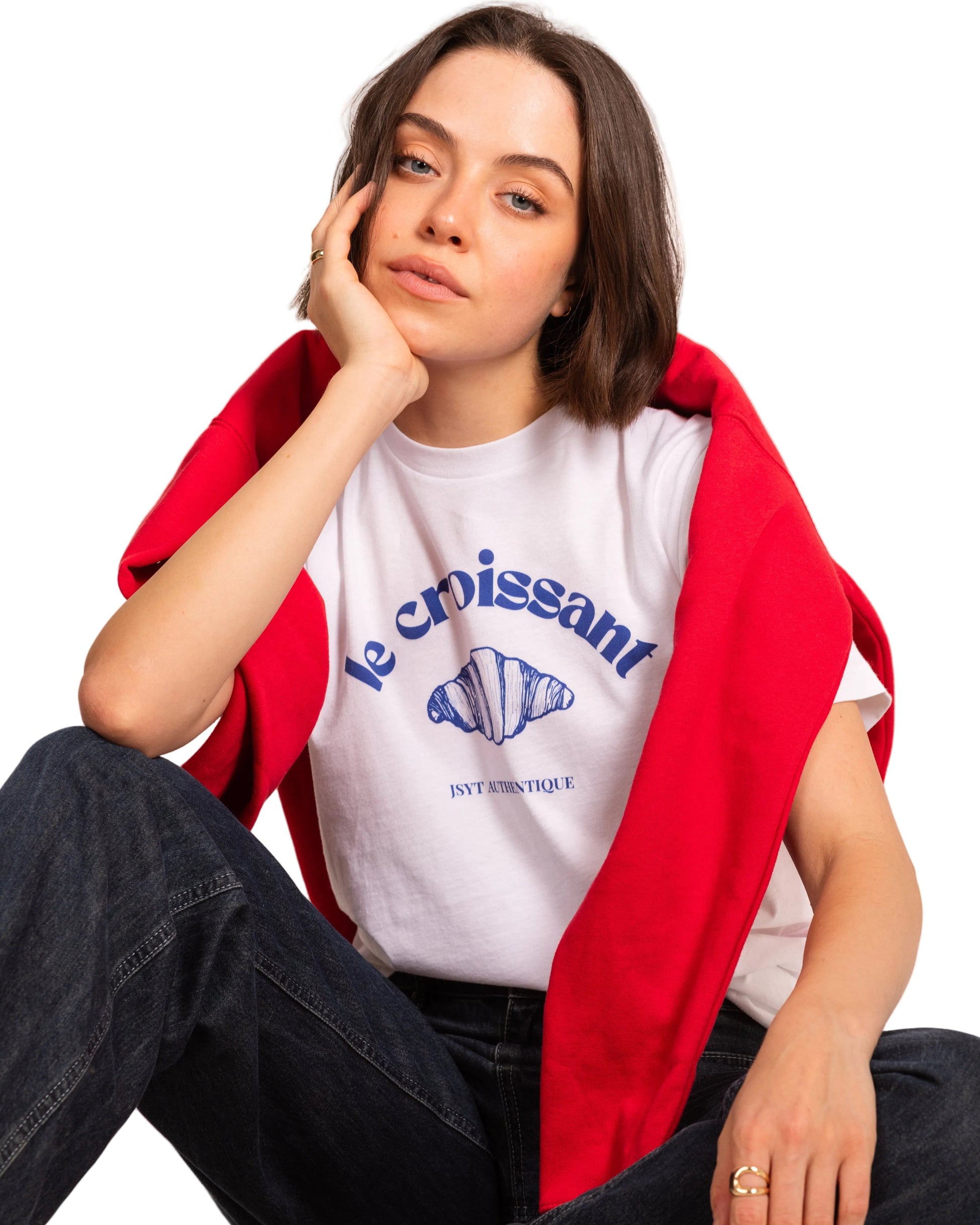 Woman wearing a white t-shirt with blue text and a red jacket, sitting on the floor.
