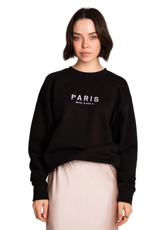 Person wearing a black sweatshirt with 'PARIS' text on a light pink background