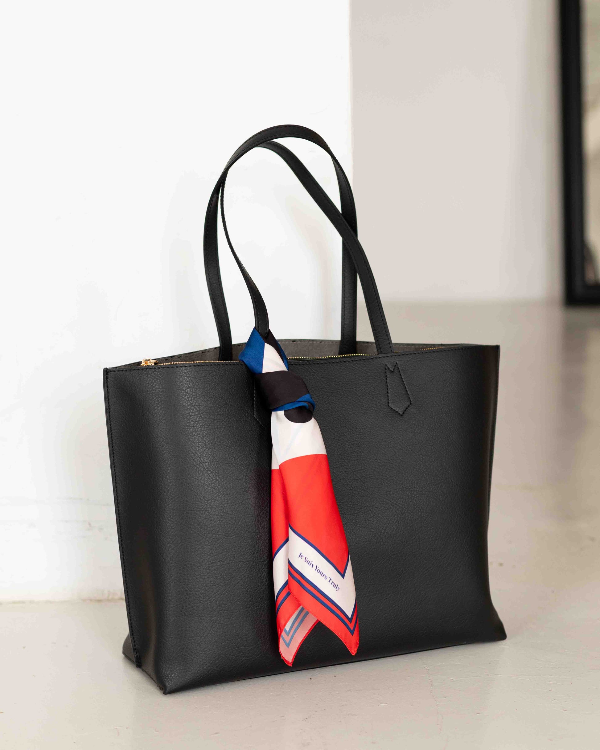 Black tote bag with a colorful scarf draped over it on a light surface.