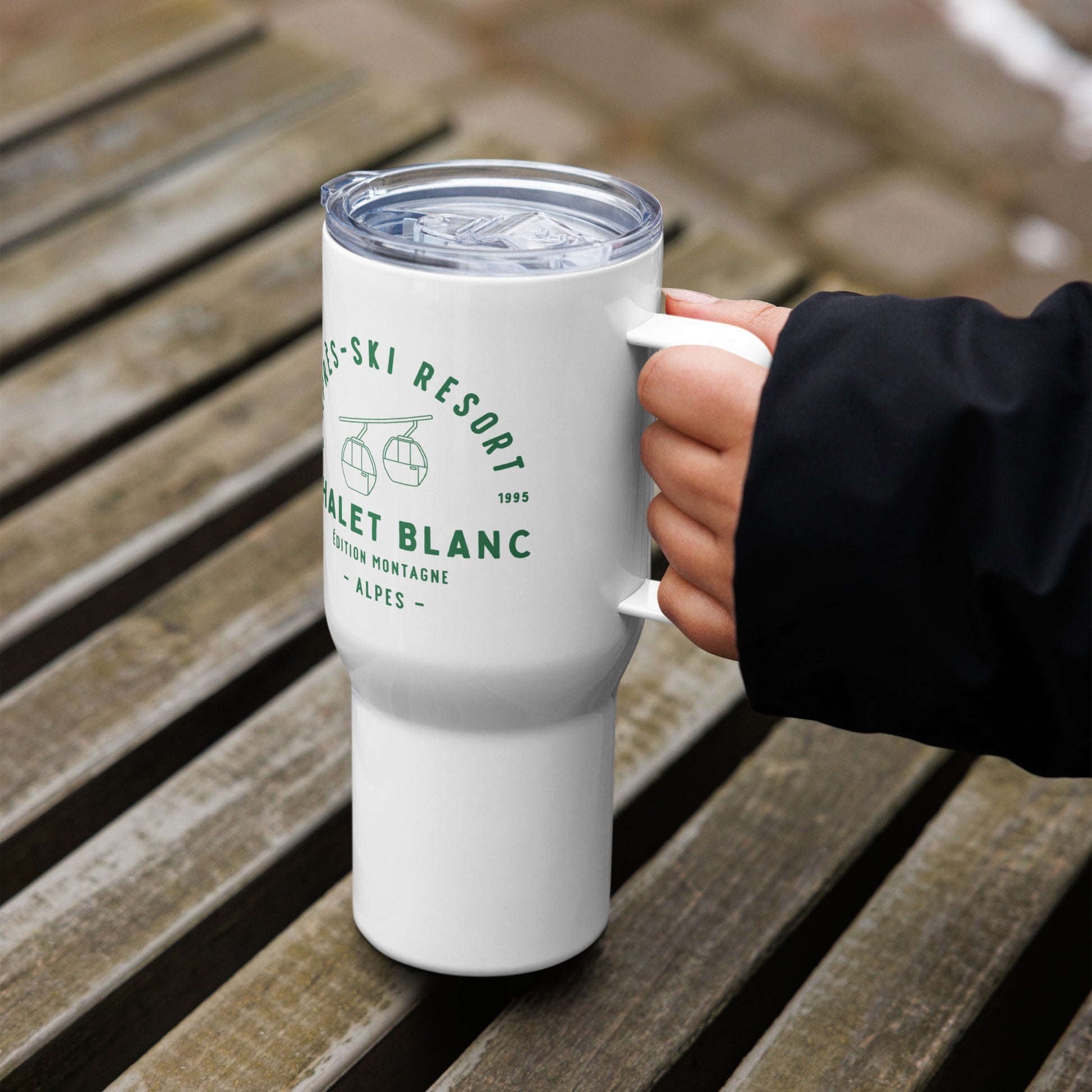 White tumbler with green text held by a person on wooden steps