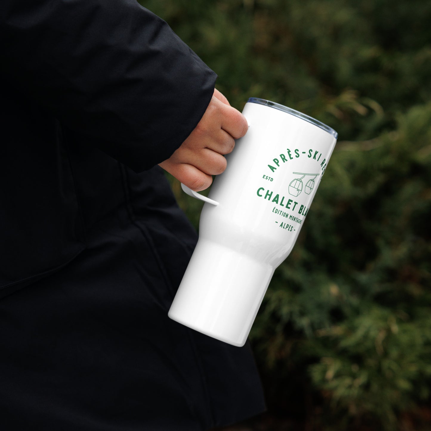 Person holding a white tumbler with text and graphics against a blurred green background