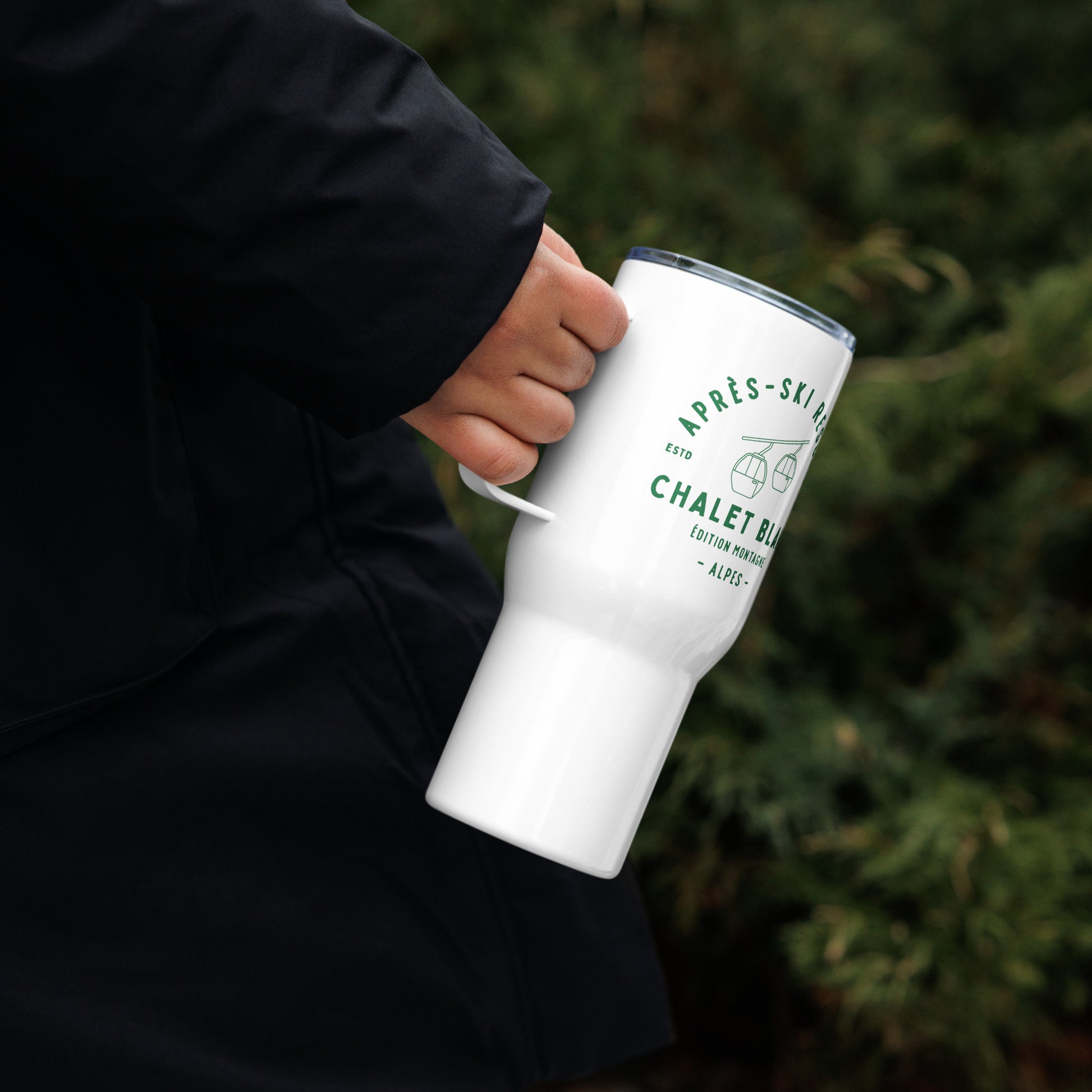 Person holding a white tumbler with text and graphics against a blurred green background