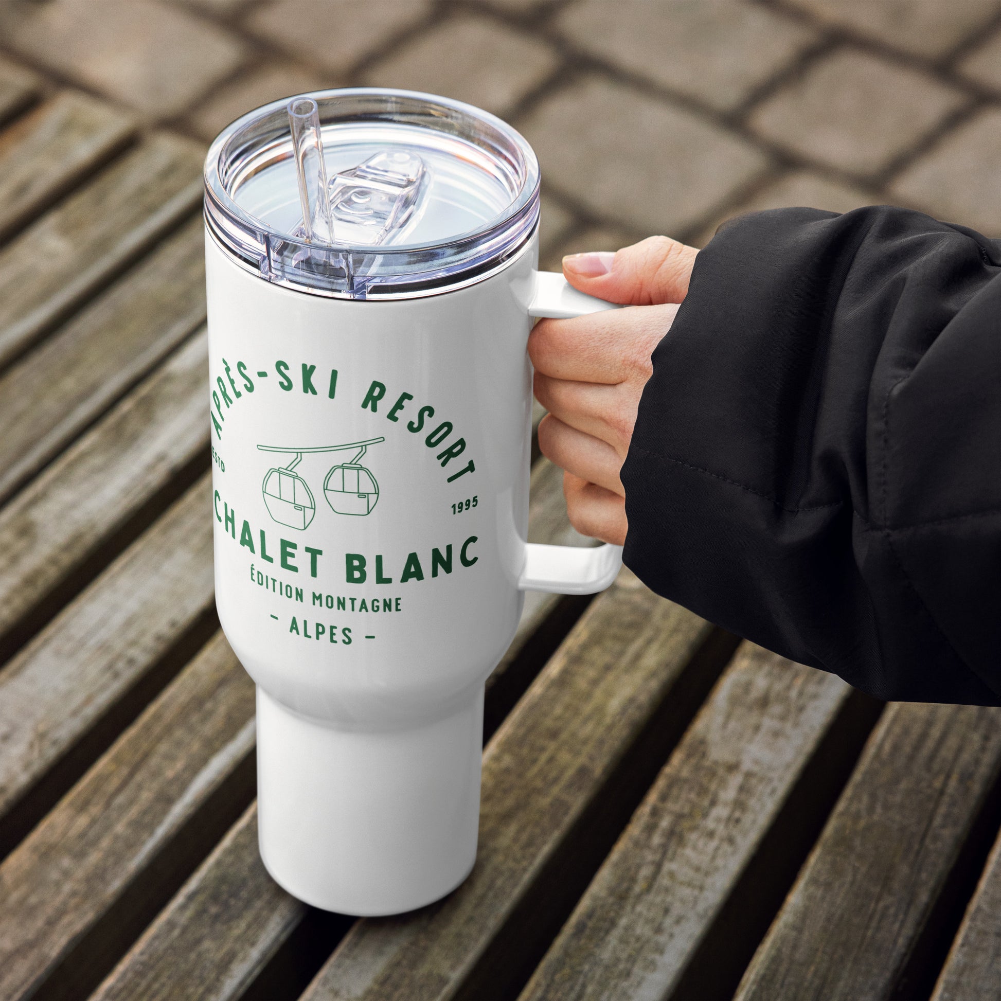 White tumbler with green text held by a person on a wooden surface